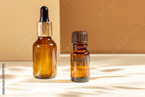 Glass cosmetic bottles with a dropper on a beige background with bright sunlight and hard shadows. The concept of natural cosmetics, natural essential oil
