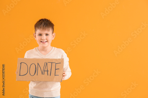 Little boy holding cardboard with text DONATE on color background