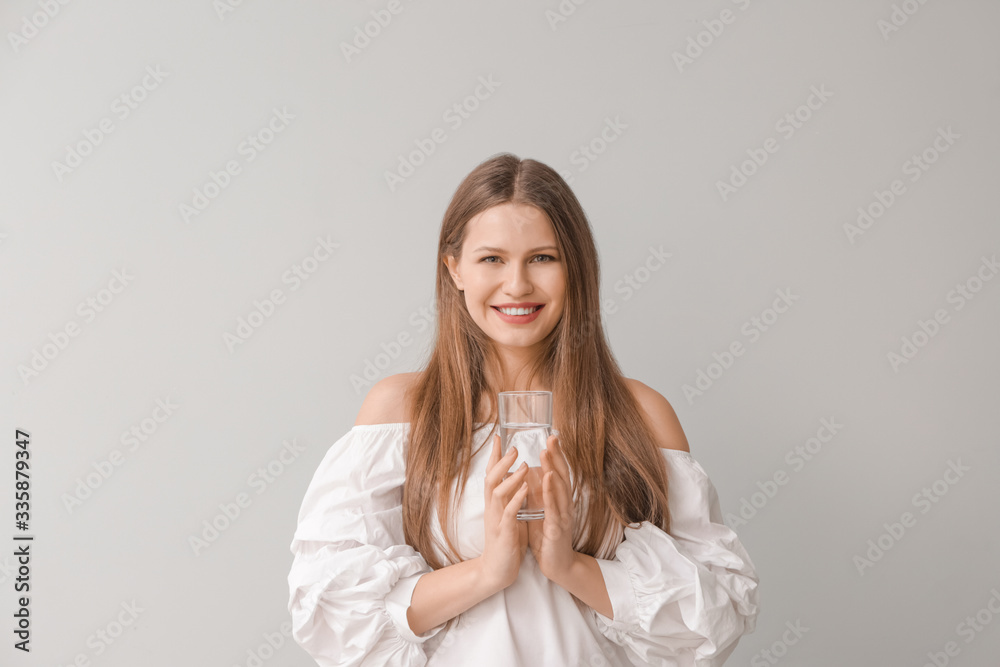 Beautiful young woman with glass of water on light background Beautiful young woman with glass of water on light background