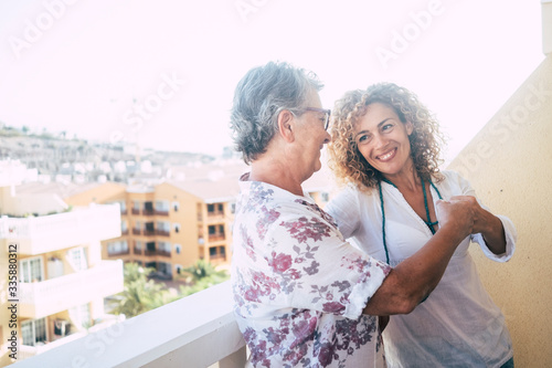 Two different ages women friends touch punch outdoor at home in the terrace with city view - concept of team and friendship or mother and daughter adult people photo