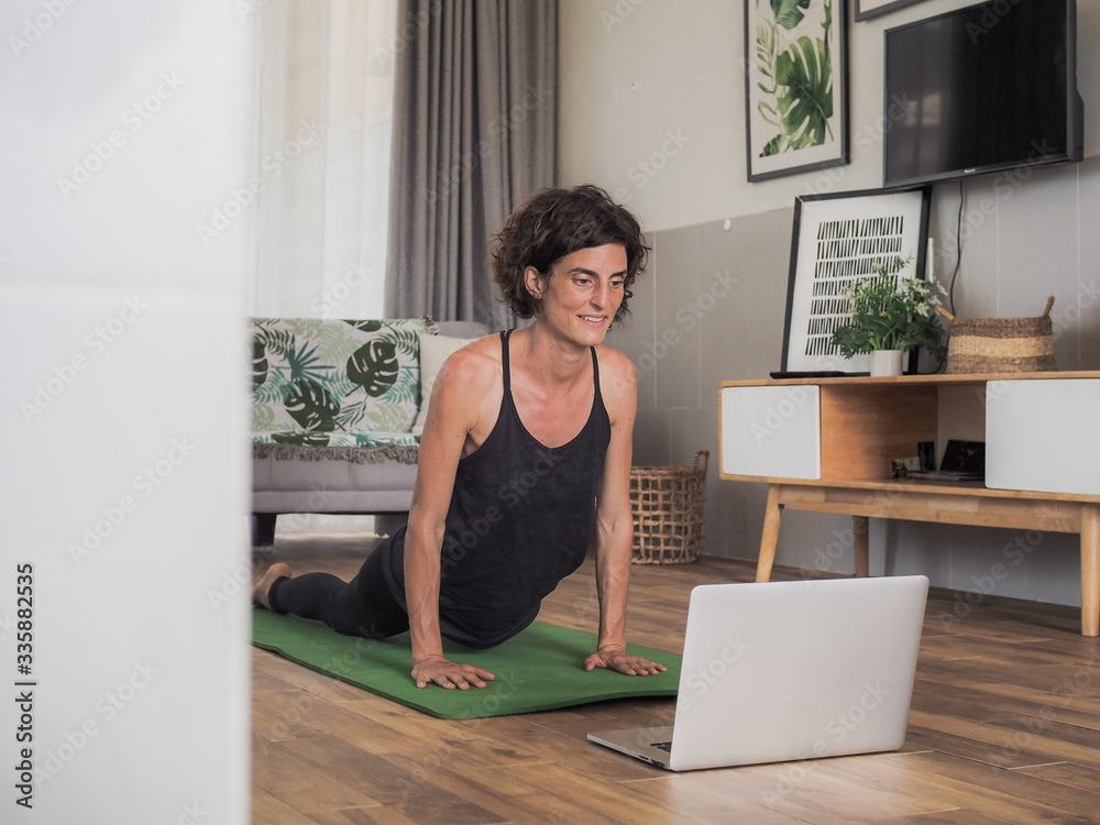 happy and smiling women looking into the laptop in doing a yoga pilates workout in her living room at home happy and smiling women looking into the laptop in doing a yoga pilates workout in her living room at home