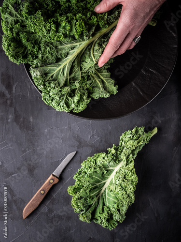 Woman's hand holding fresh green kale leaves in black bowl and photo