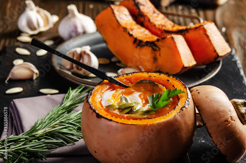 Pumpkin shell with homemade rustic pumpkin soup with seeds on slate tray with spices aside photo