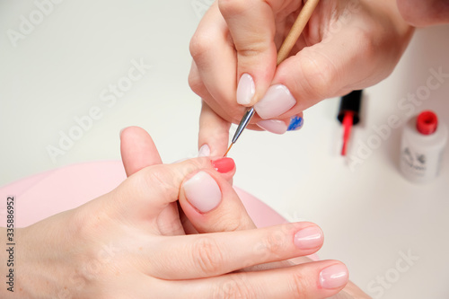 The manicure master applies a shiny nail Polish to the client s nails in a beauty salon. drawing a heart on the client s nails. Close up.