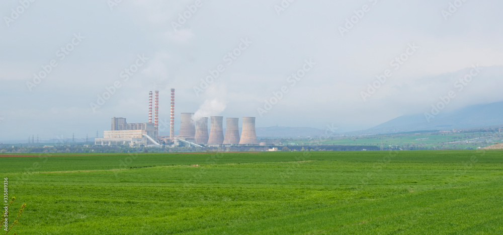 Nuclear power plant with green field and big blue clouds