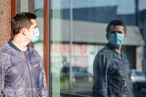 Young man in protective mask looking at his reflection at the street.