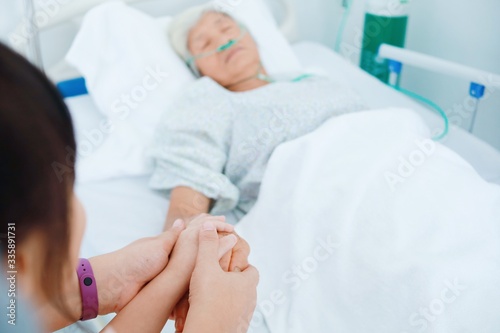 Close up Grandchild and mother holding elderly woman hands in hospital room.