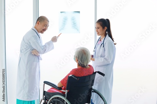 Doctor And nurse examining x-ray film to elderly woman in hospital room.