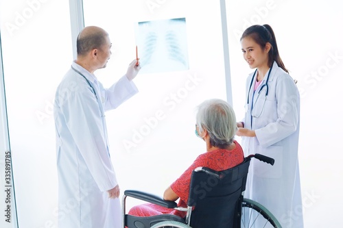 Doctor And nurse examining x-ray film to elderly woman in hospital room.