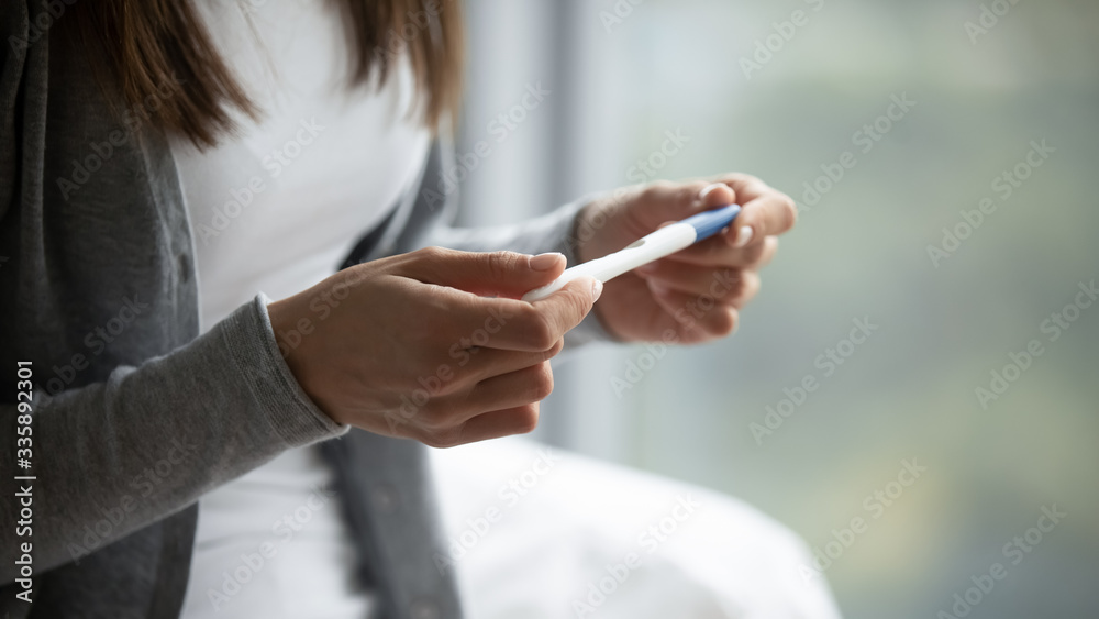 Close up of young woman hold in hands positive or negative pregnancy test thinking pondering, millennial female expecting baby undergo fertility infertility treatment, IVF, future maternity concept