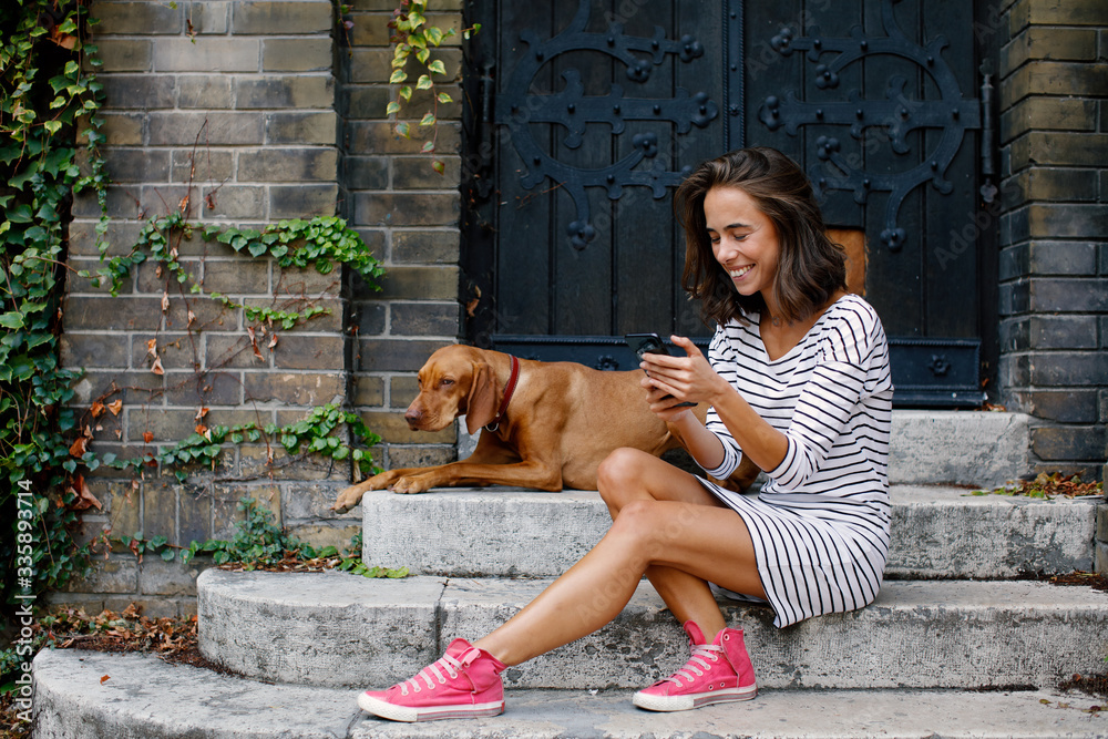 Young woman using smartphone with her dog in the backyard