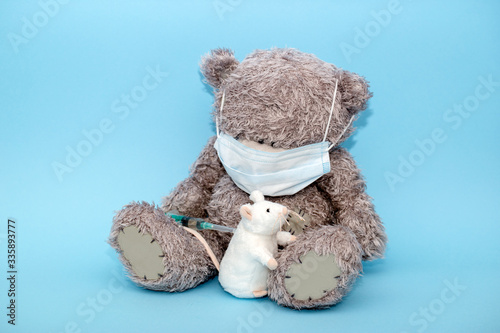 Grey toy bear in mask wants to give a shot to a white rat