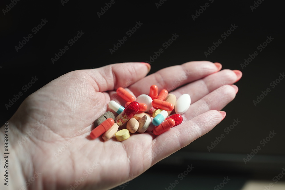 Close-up of a woman's hand on a dark background, holding a variety of different tablets and pills. Close-up of a woman's hand on a dark background, holding a variety of different tablets and pills.
