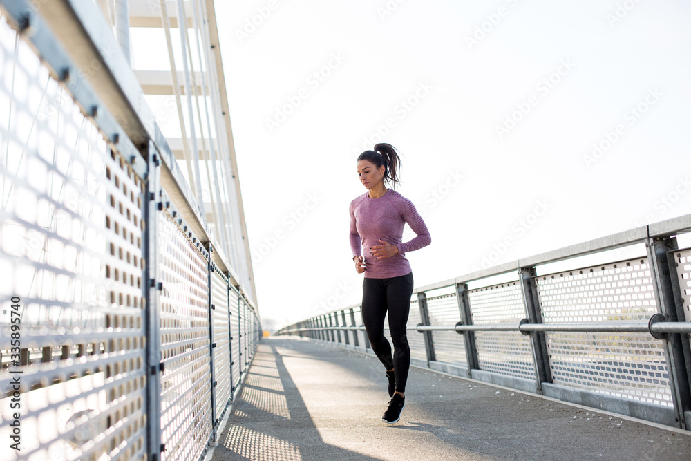 Beautiful fit woman in good shape jogging alone on city bridge. Beautiful fit woman in good shape jogging alone on city bridge.