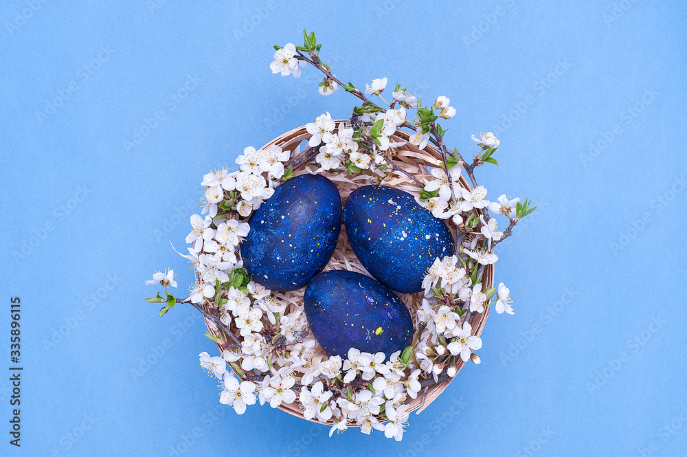 Blue easter eggs in a basket with flowers on a blue background. Horizontal photograph. Top view