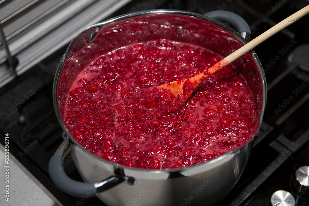 Cooking raspberry jam in a saucepan. Wooden spoon in a saucepan.