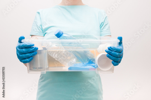 woman in a light blue t-shirt in blue disposable gloves holds a plastic container with waste for recycling, waste-free life style, waste sorting concept