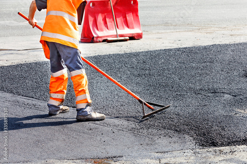 A road service worker smooths hot asphalt with a metal level manually when repairing a road.