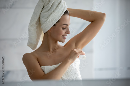 Millennial female wrapped in towel after shower use antiperspirant or deodorant after bath at home, young woman take care of armpit skin do daily beauty treatment in bathroom, hygiene concept photo