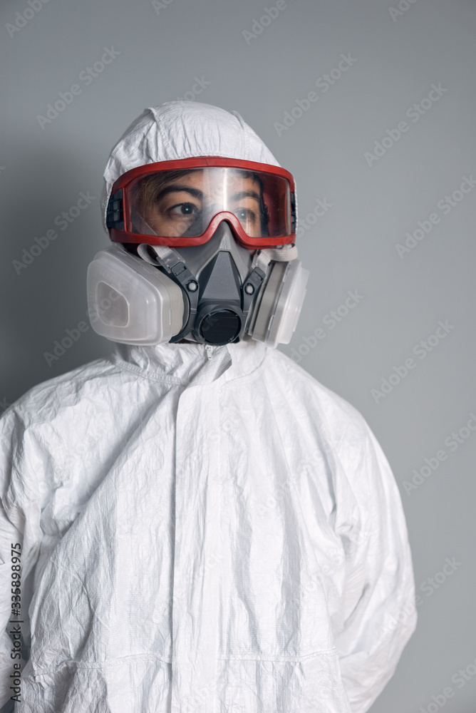 Portrait of woman in lab coat, nitrile gloves, goggles, face mask and NBC protective suit with gray background.