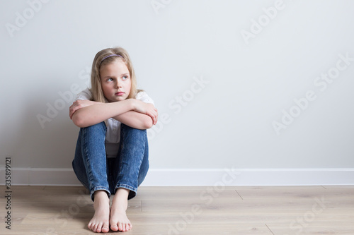 Girl 10 years old sitting on the floor in the room. Barefoot. He looks away, dreams. Grey background.