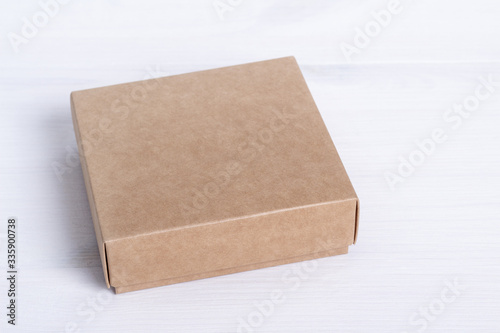 Blank cardboard box package isolated on white wood background. Craft paper box side view. Small square closed cardboard. Shipping eco package. Delivery pack. Gift idea, eco-lifestyle. Natural concept