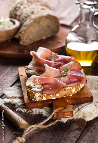 Bruschettas with cream cheese, prosciutto and rosemary on cutting board and wooden table