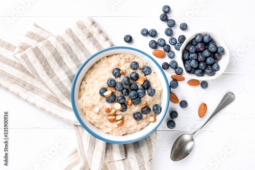 Oatmeal porridge with blueberries, almond nuts, table top view on white background. Healthy food, vegan vegetarian diet