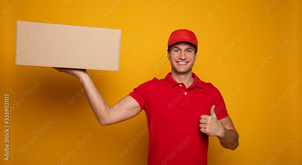 Handsome young happy courier or delivery man in red uniform is posing isolated on yellow background. Handsome young happy courier or delivery man in red uniform is posing isolated on yellow background.