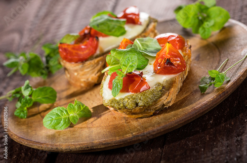 Bruschetta with tomatoes, mozzarella cheese, pesto and fresh basil on wooden background.