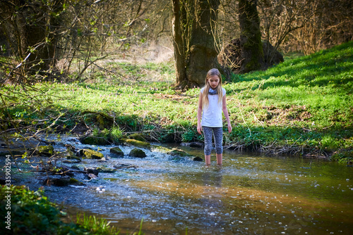 Child cute blond girl playing in the creek. Girl walking barefoot in forest stream and exploring nature. Summer children fun. Children summer activities 