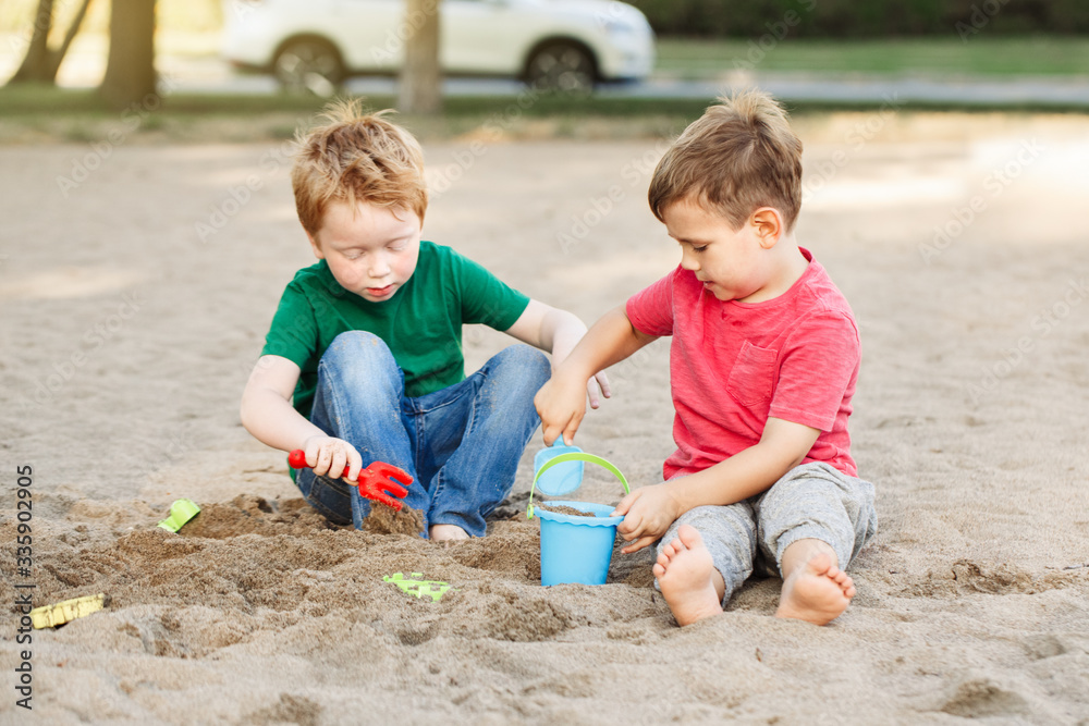 Two Caucasian children sitting in sandbox playing with beach toys. Little boys friends having fun together on a playground. Summer outdoor activity for kids. Leisure time lifestyle childhood. Two Caucasian children sitting in sandbox playing with beach toys. Little boys friends having fun together on a playground. Summer outdoor activity for kids. Leisure time lifestyle childhood.
