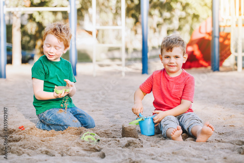 Two Caucasian children sitting in sandbox playing with beach toys. Little boys friends having fun together on a playground. Summer outdoor activity for kids. Leisure time lifestyle childhood.