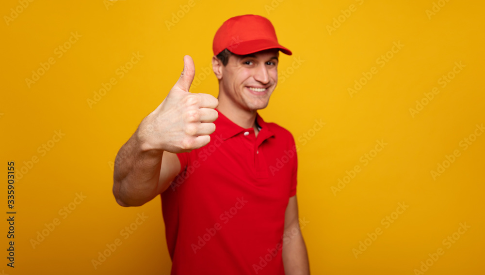 Handsome young happy courier or delivery man in red uniform is posing isolated on yellow background. Handsome young happy courier or delivery man in red uniform is posing isolated on yellow background.