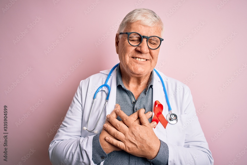 Senior handsome hoary doctor man wearing stethoscope and red HIV ribbon on coat smiling with hands on chest with closed eyes and grateful gesture on face. Health concept. Senior handsome hoary doctor man wearing stethoscope and red HIV ribbon on coat smiling with hands on chest with closed eyes and grateful gesture on face. Health concept.