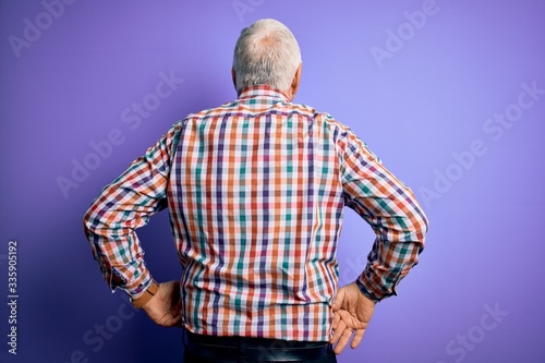 Senior handsome hoary man wearing casual colorful shirt over isolated purple background standing backwards looking away with arms on body © Krakenimages.com