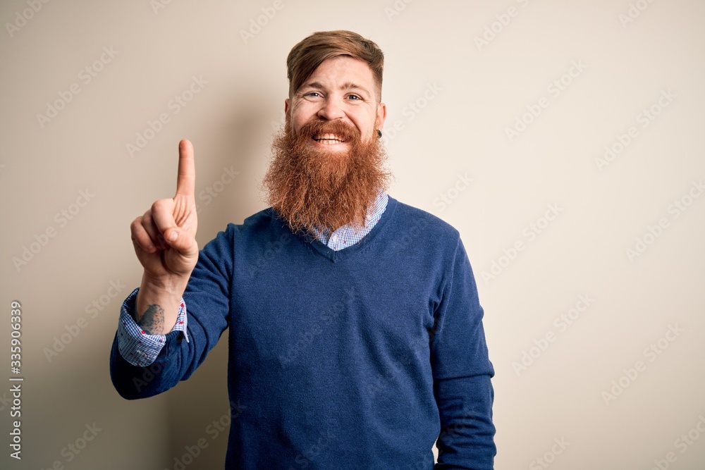 Handsome Irish redhead business man with beard standing over isolated background showing and pointing up with finger number one while smiling confident and happy. Handsome Irish redhead business man with beard standing over isolated background showing and pointing up with finger number one while smiling confident and happy.