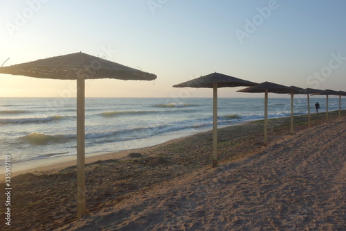 Row of reed parasols along sea shore and single man walking  in Vama Veche  Romania  early in the morning