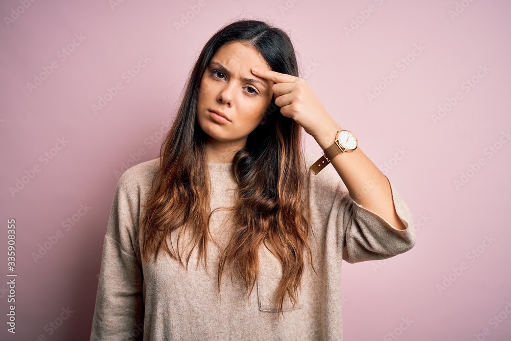 Young beautiful brunette woman wearing casual sweater standing over pink background pointing unhappy to pimple on forehead, ugly infection of blackhead. Acne and skin problem Young beautiful brunette woman wearing casual sweater standing over pink background pointing unhappy to pimple on forehead, ugly infection of blackhead. Acne and skin problem