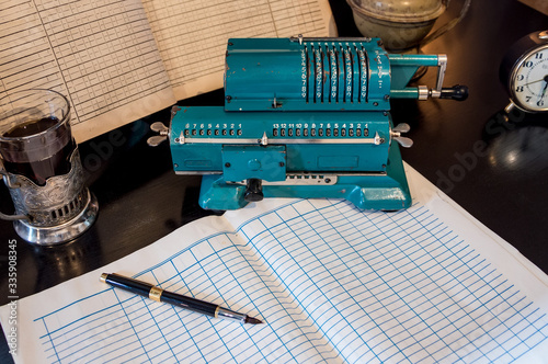 An old mechanical calculator, an arithmetic counter, accounting books, a watch, and a pen on a black table.