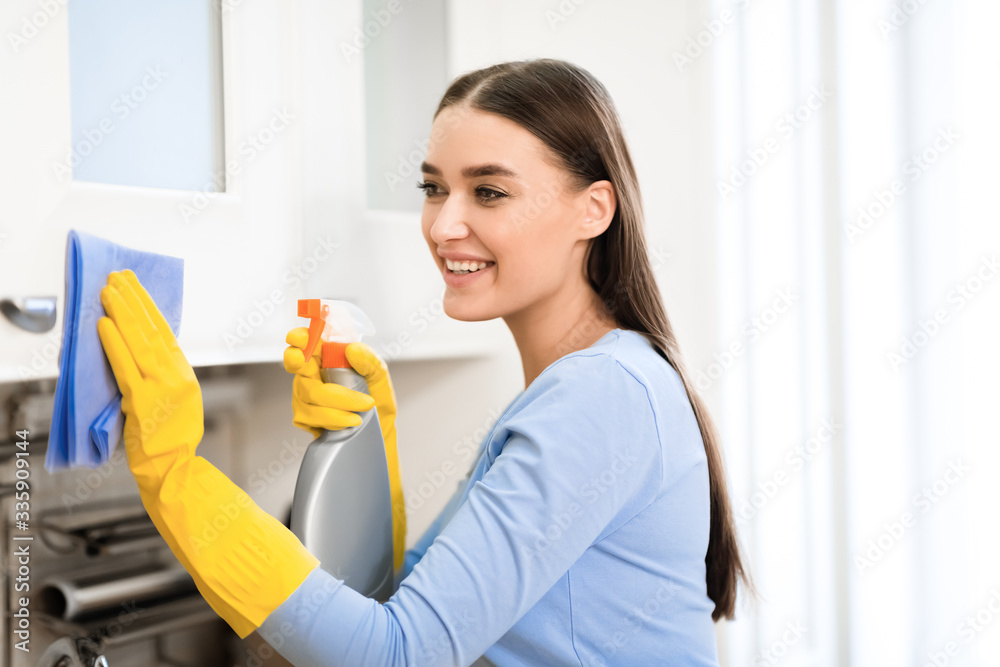 Young woman cleaning kitchen furniture using spray Young woman cleaning kitchen furniture using spray