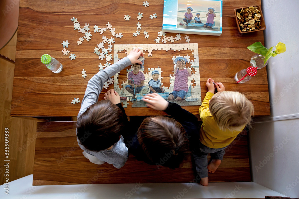 Three children, boys, assembling puzzle with their picture from the beach, playing at home - obrazy, fototapety, plakaty 