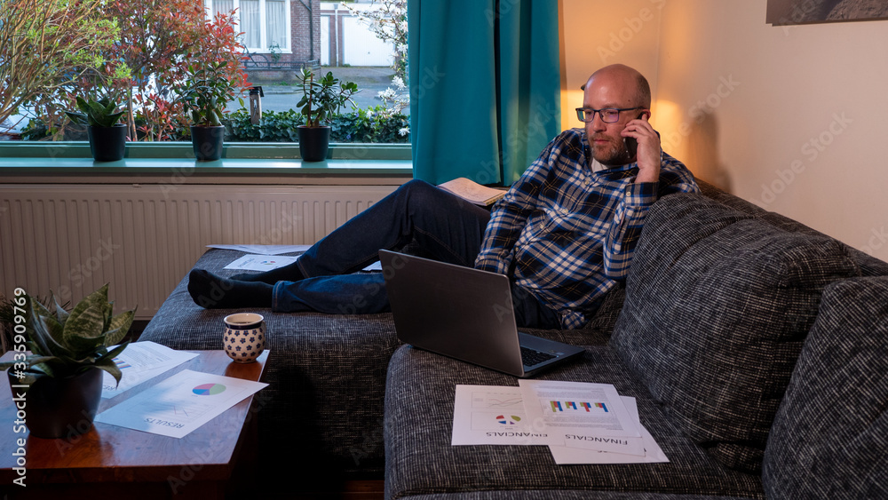 Fototapeta premium Man with beard calling with smartphone at home from the couch. Businessman working at home with paperworks and documents on the couch.