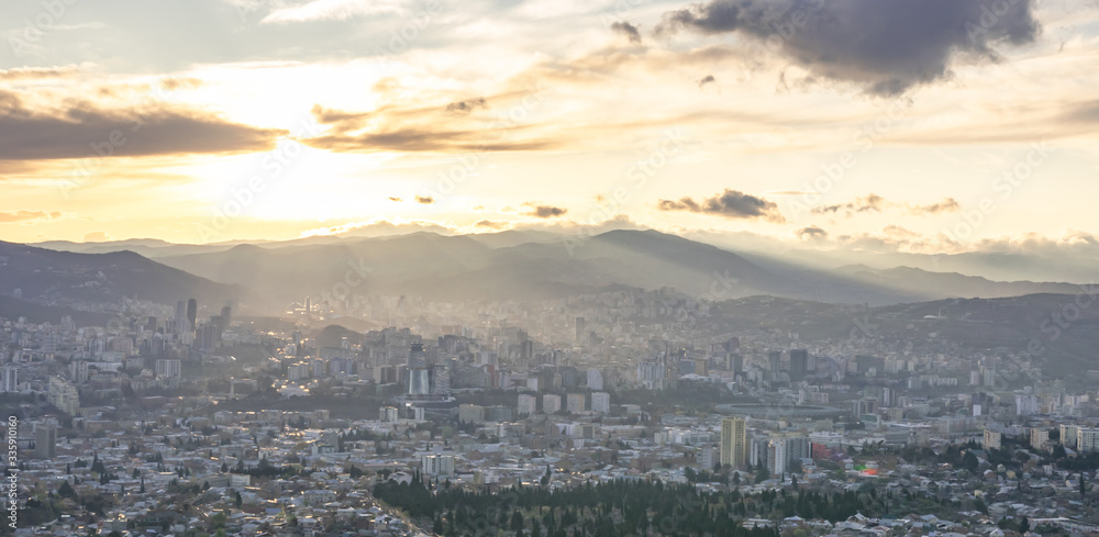 Dramatic Aerial view to Tbilisi city buildings from far distance with caucasus mountains in the background  uring the sunset.2020
