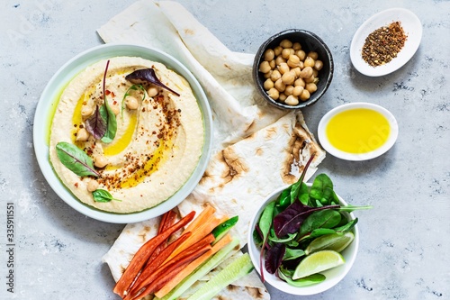 Classic hummus in a bowl with herbs, paprika, olive oil, pita bread, vegetable sticks and lettuce on a blue (gray) background.Healthy vegan food.A dish of Middle Eastern cuisine.Healthy eating concept