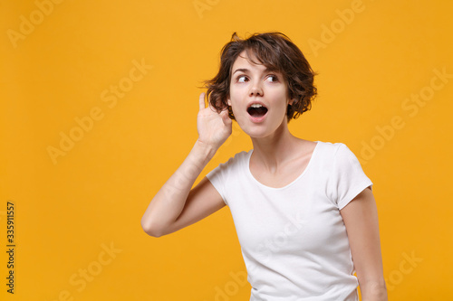 Принти на полотні Curious young brunette woman girl in white t-shirt posing isolated on yellow orange wall background studio portrait