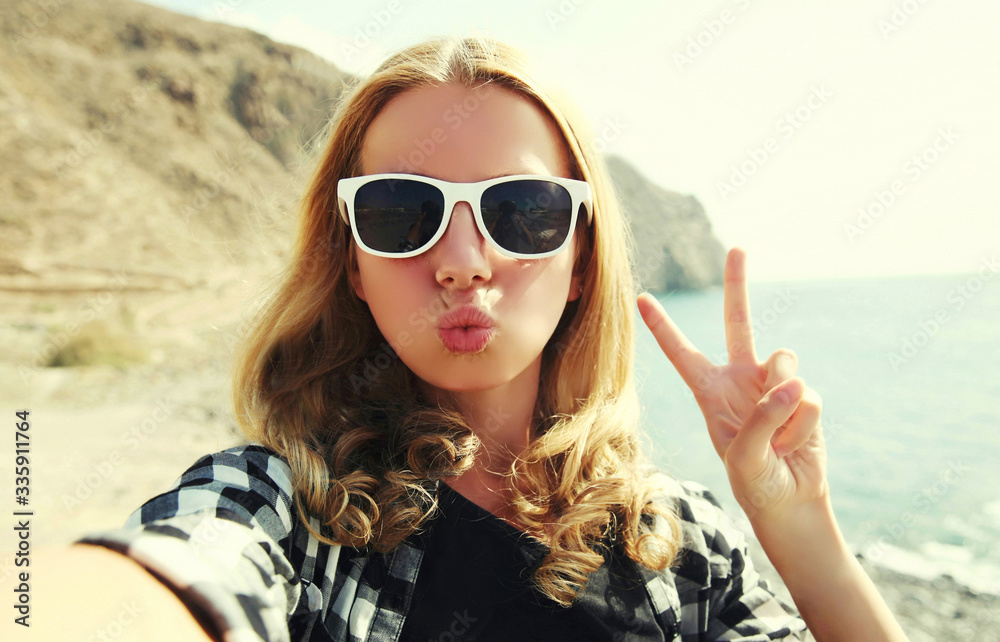 Portrait of happy woman blowing lips sending sweet air kiss stretching hand for taking selfie over sea background Portrait of happy woman blowing lips sending sweet air kiss stretching hand for taking selfie over sea background
