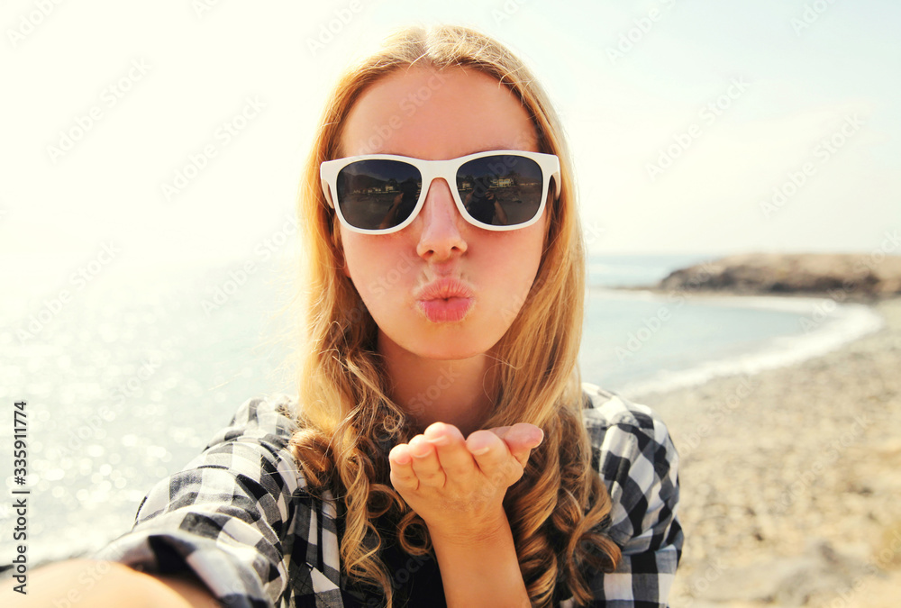 Portrait of happy woman blowing lips sending sweet air kiss stretching hand for taking selfie over sea background Portrait of happy woman blowing lips sending sweet air kiss stretching hand for taking selfie over sea background