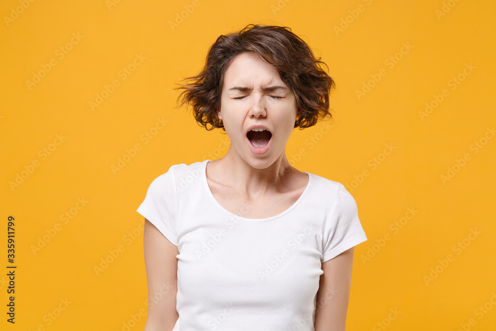 Frustrated young brunette woman girl in white t-shirt posing isolated on yellow orange wall background studio portrait. People lifestyle concept. Mock up copy space. Keeping eyes closed, screaming. Frustrated young brunette woman girl in white t-shirt posing isolated on yellow orange wall background studio portrait. People lifestyle concept. Mock up copy space. Keeping eyes closed, screaming.