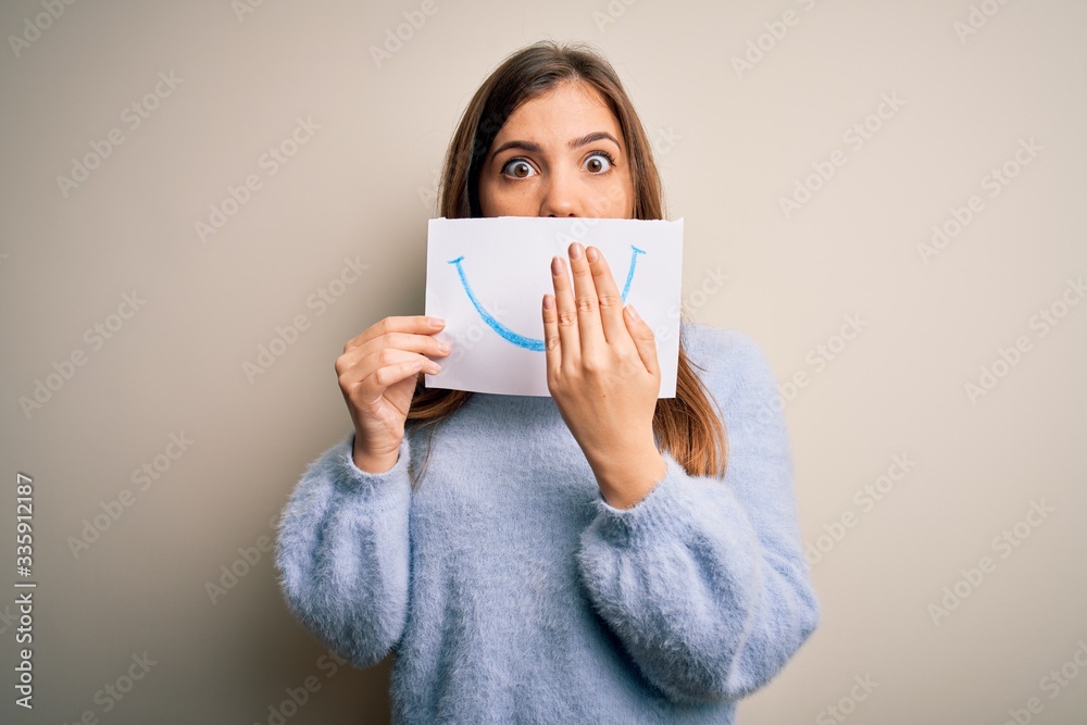 Young blonde woman holding funny smile drawing on mouth as happy expression cover mouth with hand shocked with shame for mistake, expression of fear, scared in silence, secret concept Young blonde woman holding funny smile drawing on mouth as happy expression cover mouth with hand shocked with shame for mistake, expression of fear, scared in silence, secret concept